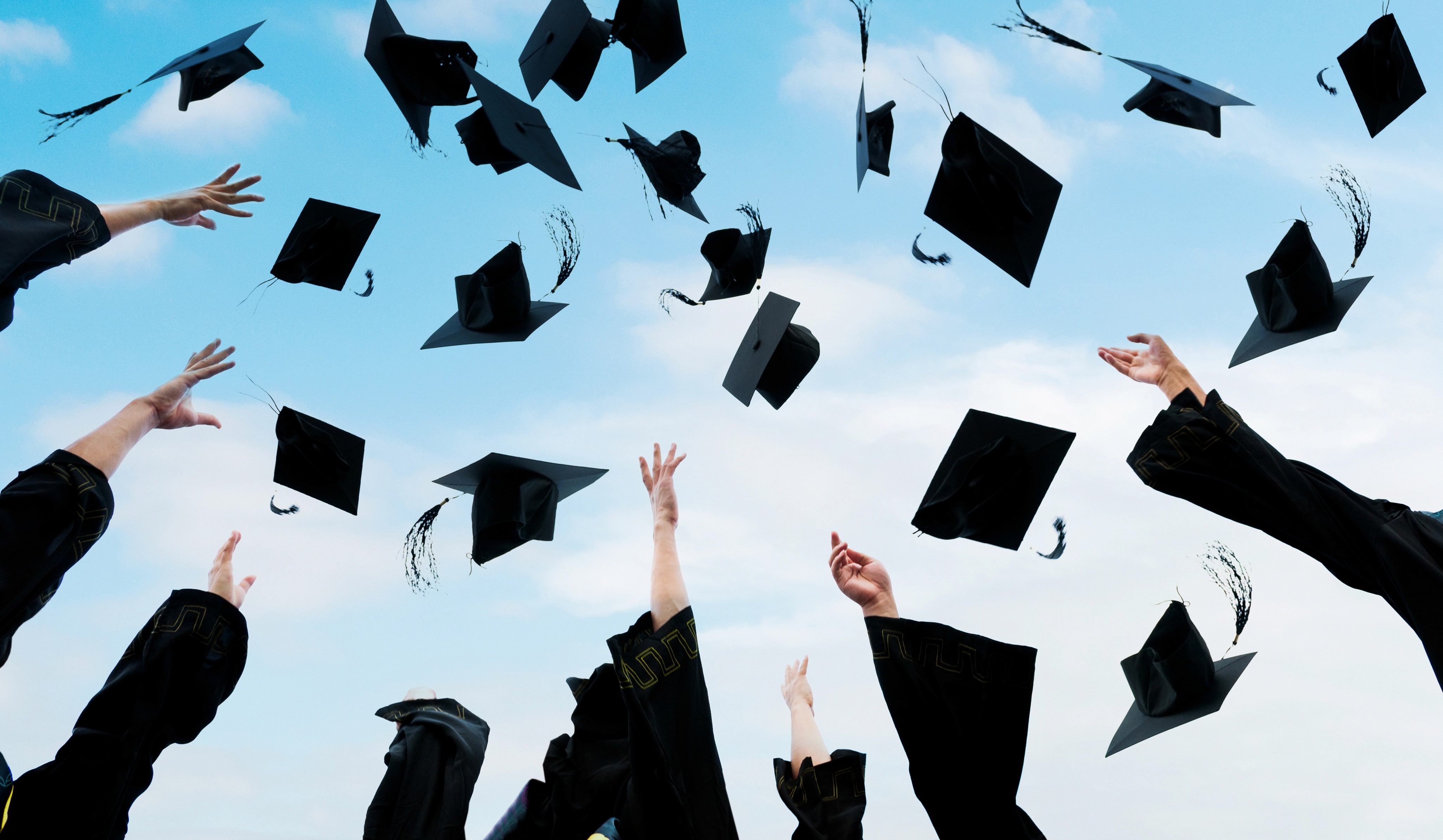 Graduates throwing mortarboard caps into a blue sky